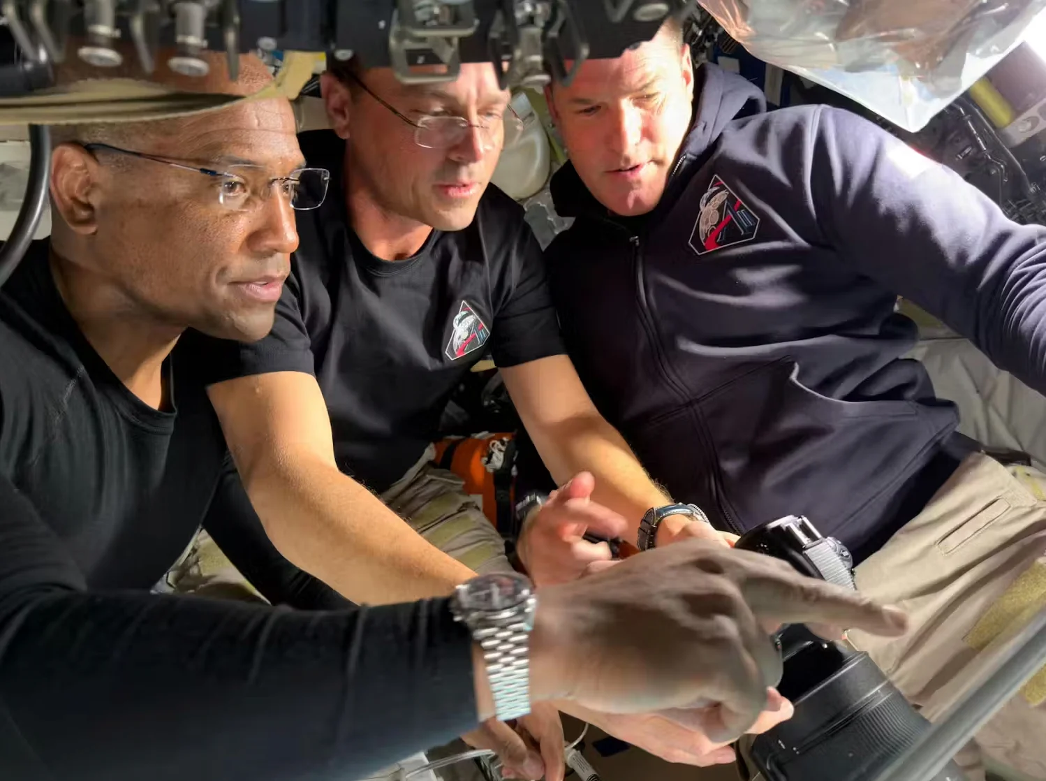 NASA: Artemis II Pilot Victor Glover, Commander Reid Wiseman, and Mission Specialist Jeremy Hansen configure their camera equipment shortly before beginning their lunar flyby observations. (NASA)
