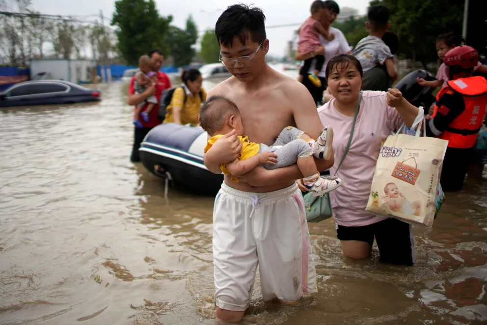Reuters: A man holding a baby wades through a flooded road following heavy rainfall in Zhengzhou, Henan province, China July 22, 2021. REUTERS/Aly Song