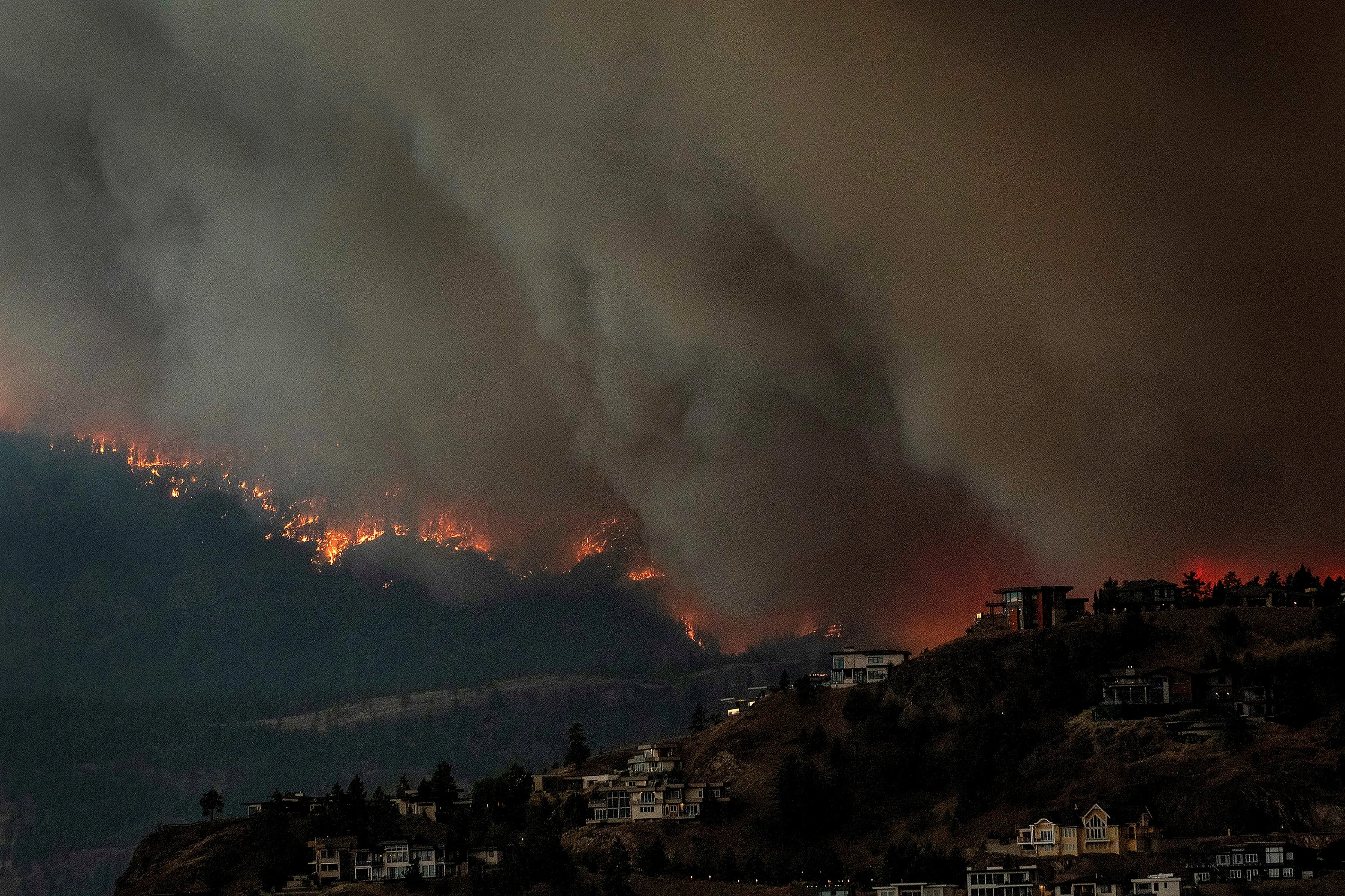 REUTERS: Smoke and flames from wildfires serve as a backdrop for homes across Okanagan Lake in West Kelowna, British Columbia, Canada, August 17, 2023. REUTERS/Dan Riedlhuber/File Photo