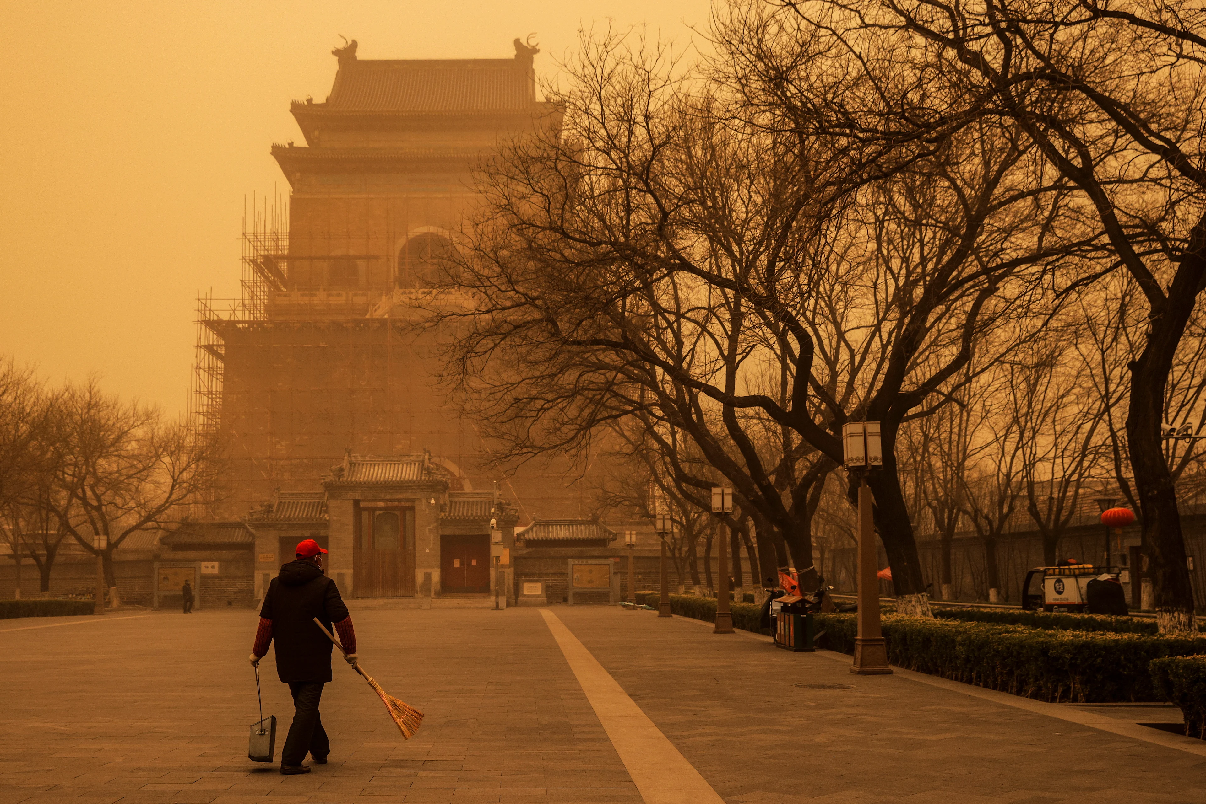 Reuters: A person walks with a broom and dustpan during morning rush hour as Beijing, China, is hit by a sandstorm, March 15, 2021. REUTERS/Thomas Peter