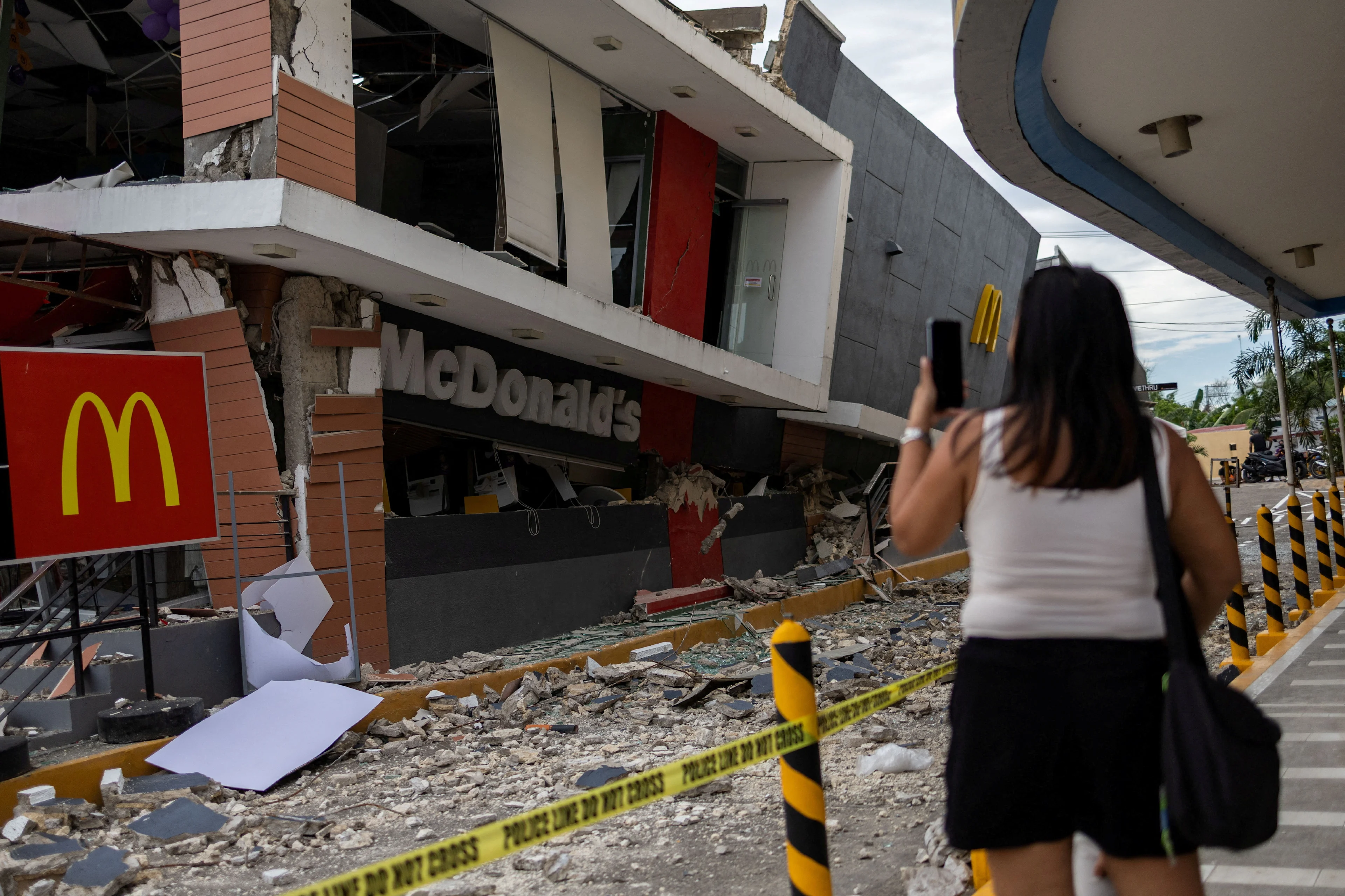 REUTERS: A woman takes a photo of a damaged Mcdonald's store in the aftermath of a magnitude 6.9 quake in Bogo, Cebu, Philippines, October 1, 2025. REUTERS/Eloisa Lopez