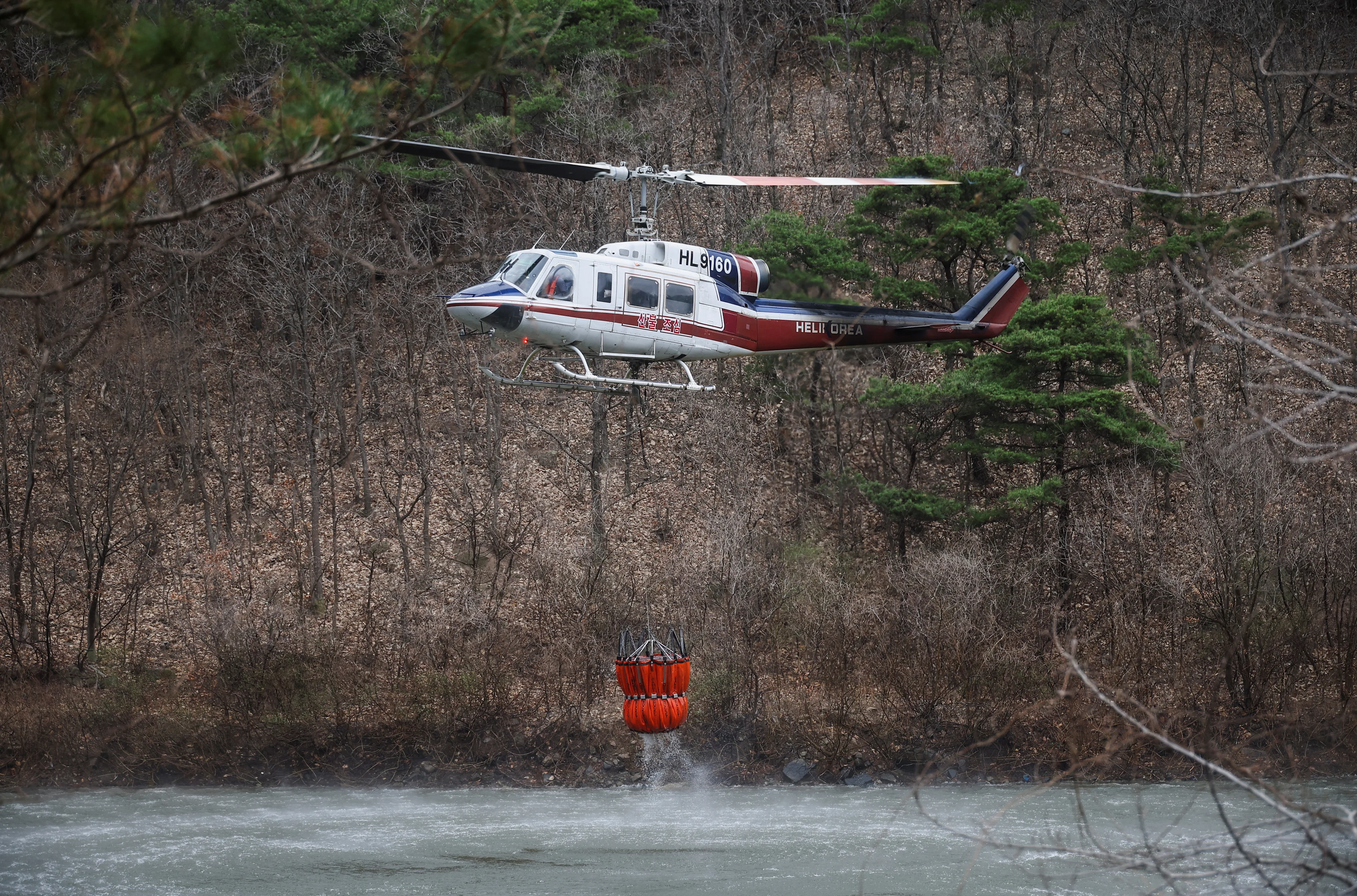 REUTERS: A firefighting helicopter picks up water from a water source during an operation as a wildfire burns, in Uiseong, South Korea, March 27, 2025. REUTERS/Kim Hong-Ji