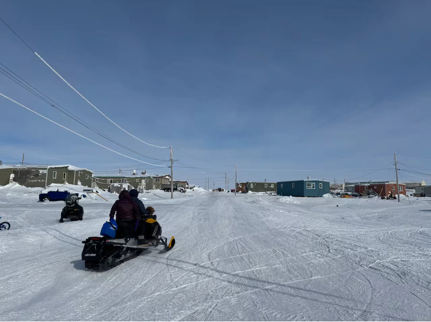 cbc: People in Gjoa Haven, Nunavut, riding a snowmobile on Apr. 16, 2026. Weather conditions are much better now, but the area was hit with multiple blizzards earlier this month. (Samuel Wat/CBC)