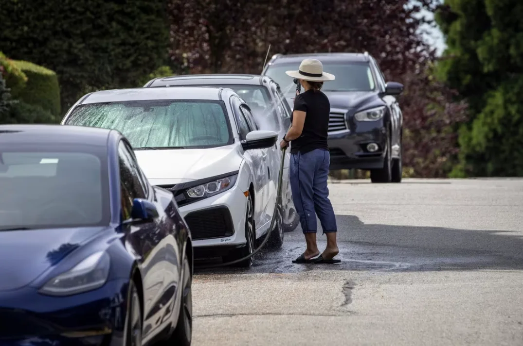 CBC: A woman washes her car with a hose on a street in Vancouver, on Aug. 11. Landscape architect Karin England says keeping lawns green in the summer can be more wasteful than people think. (Ben Nelms/CBC)