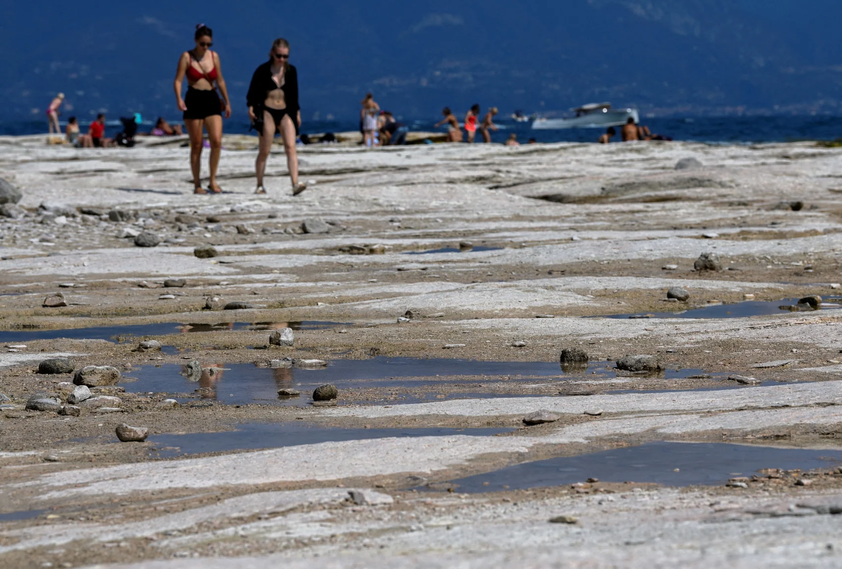 People walk as underwater rocks emerge from the water of Lake Garda after northern Italy experienced the worst drought in 70 years in Sirmione, Italy, August 16, 2022. (REUTERS/Flavio Lo Scalzo/File Photo)