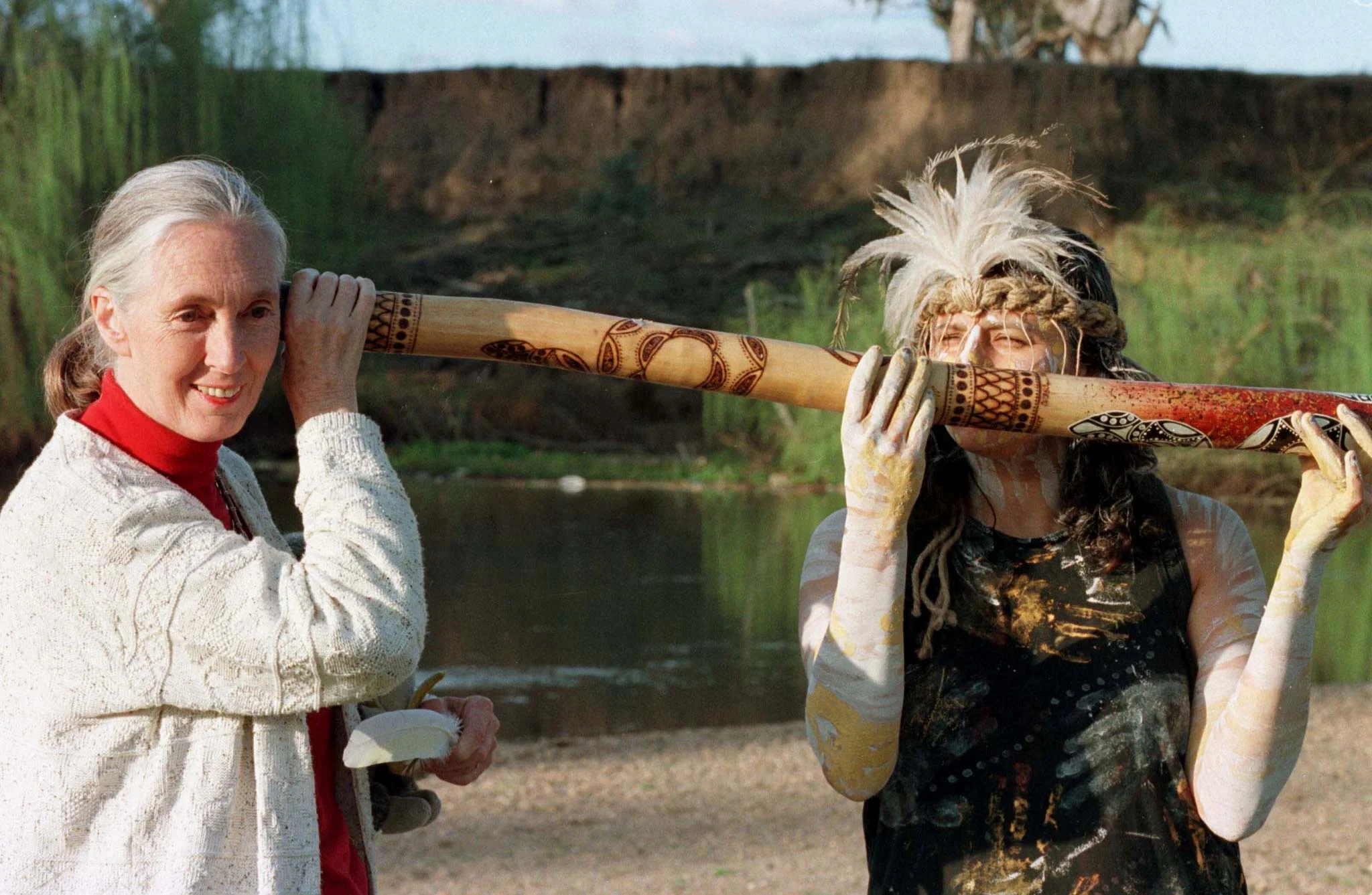 Reuters: FILE PHOTO: England's Dr Jane Goodall (L), chimpanzee researcher and naturalist, listens to sounds from the inside of a traditional Aboriginal Didjeridoo with Aboriginal dancer Dianne McNaboe of the Wiradjuri Tribe after a womens cleaning ceremony which was performed by McNaboe on the banks of MacQuarie River at Dubbo in western New South Wales, September 3. Goodall visited the Western Plains Zoo is in Australia to raise the awareness that Chimpanzee numbers in the wild have plummeted 75 percent in 10 years leaving only about 250,000 in their homeland's of Central and West Africa. AUSTRALIA/File Photo