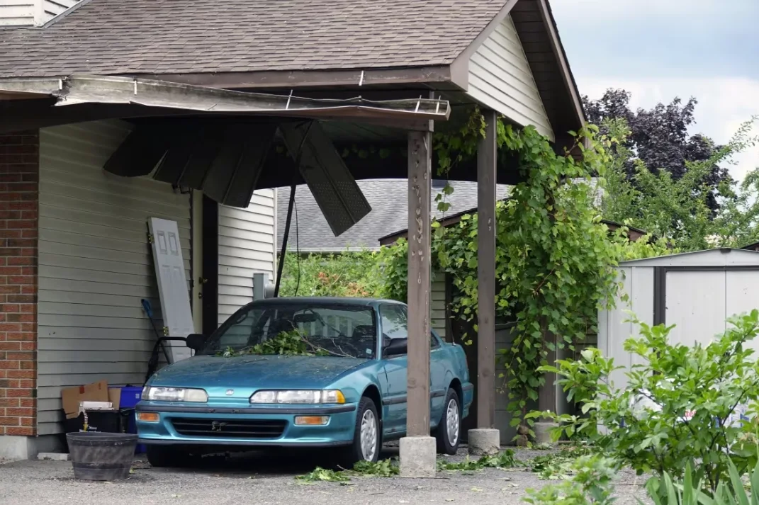 CBC: A car covered in tree branches sits below a car port that's been damaged by the tornado that hit Barrhaven, Ont. on July 13, 2023. (Dan Taekema/CBC)