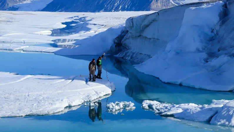CBC Researchers Joseph Shoapik, left, and Jérémie Bonneau measure the temperature and salinity of the water through rifts in the Milne Ice Shelf in 2022. The ice shelf broke apart, forming such rifts, in 2020. (Cameron Fitzpatrick)