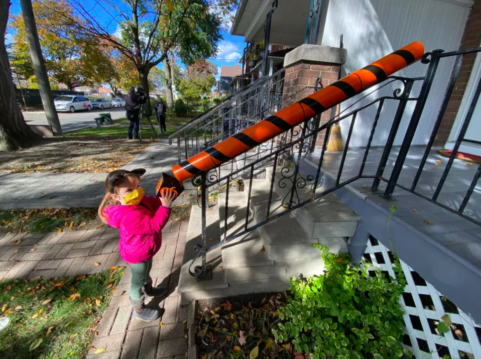 Made out of basic PVC pipes, the chute is attached to a stair bannister in front of a house so residents can stand at the top and send down treats to kids, who wait at the bottom with their bags to ensure physical distancing. (Paul Borkwood/CBC)