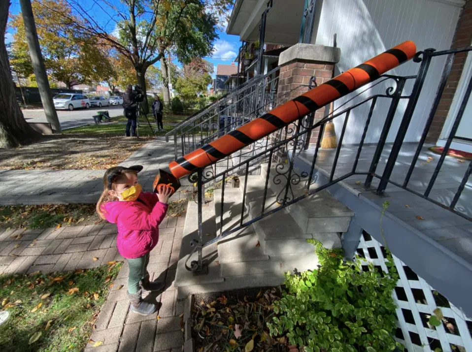 Made out of basic PVC pipes, the chute is attached to a stair bannister in front of a house so residents can stand at the top and send down treats to kids, who wait at the bottom with their bags to ensure physical distancing. (Paul Borkwood/CBC)