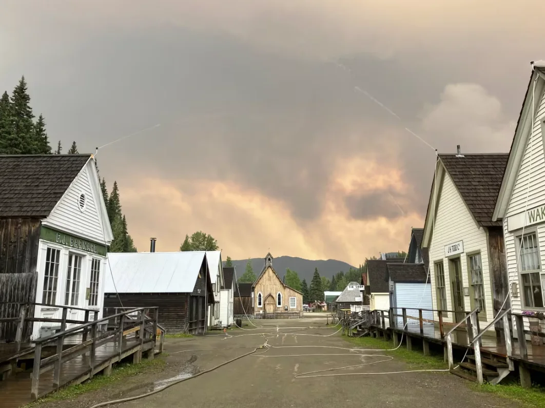 CBC: Hoses are seen spraying water over houses in the historic gold rush community of Barkerville, B.C., as it is threatened by wildfires. (B.C. Wildfire Service)