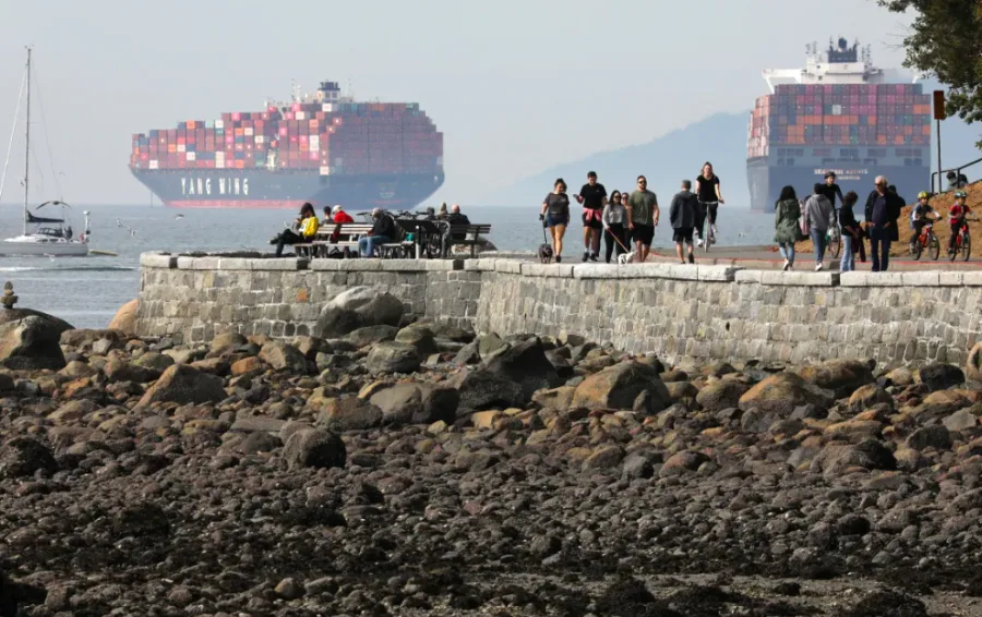 People walk on Stanley Park’s seawall near container ships anchored in English Bay in Vancouver. The Port of Vancouver has partnered with two American ports to try to develop 'green corridors' to spur the development of low-emission fuels. (Chris Helgren/Reuters)