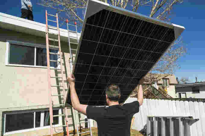 Workers moving solar modules while installing solar panels on a residential roof. (powerofforever/ E+/ Getty Images)