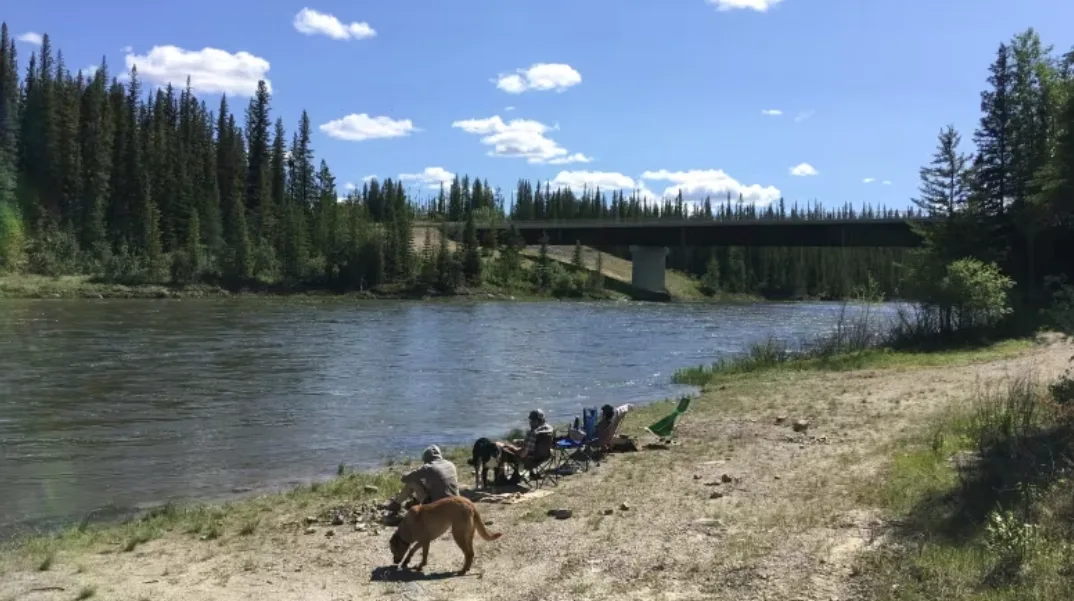 CBC: People sitting along the shores of the Kakisa River in 2020, enjoying the summer heat. The river flows from Kakisa Lake, where fish plumped up after the 2014 wildfire. (Walter Strong/CBC)