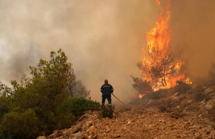 A firefighter tries to extinguish a wildfire burning near the village of Kandyli, near Athens, Greece, July 19, 2023. REUTERS/Stelios Misinas