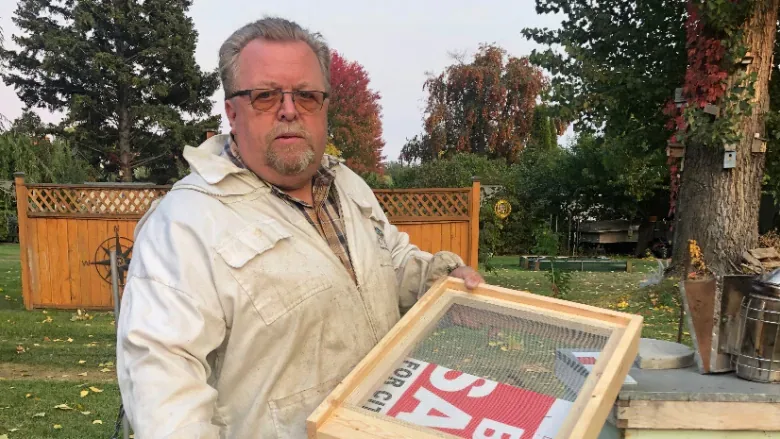 kamloops-beekeeper-murray-willis-holds-a-bee-box-screen-bottom-inserted-with-an-election-sign/Submitted by Murray Willis via CBC