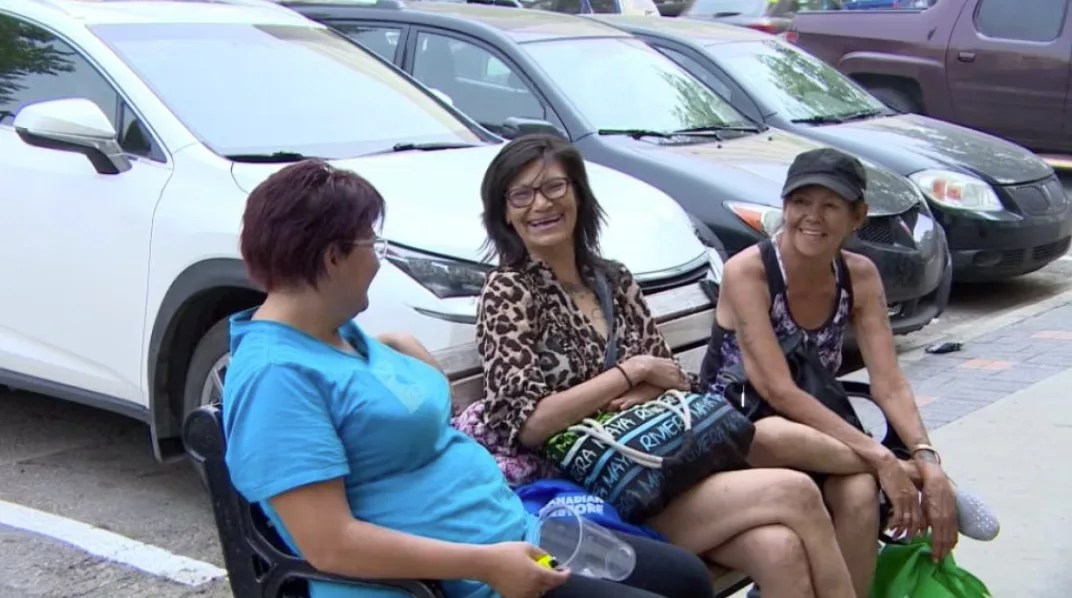 CBC: Sophia Dawn Nanaqewetung, middle, sits in shade with her friends. A someone living on the streets, she says there are few places to avoid the wildfire smoke. (Travis Reddaway/CBC)